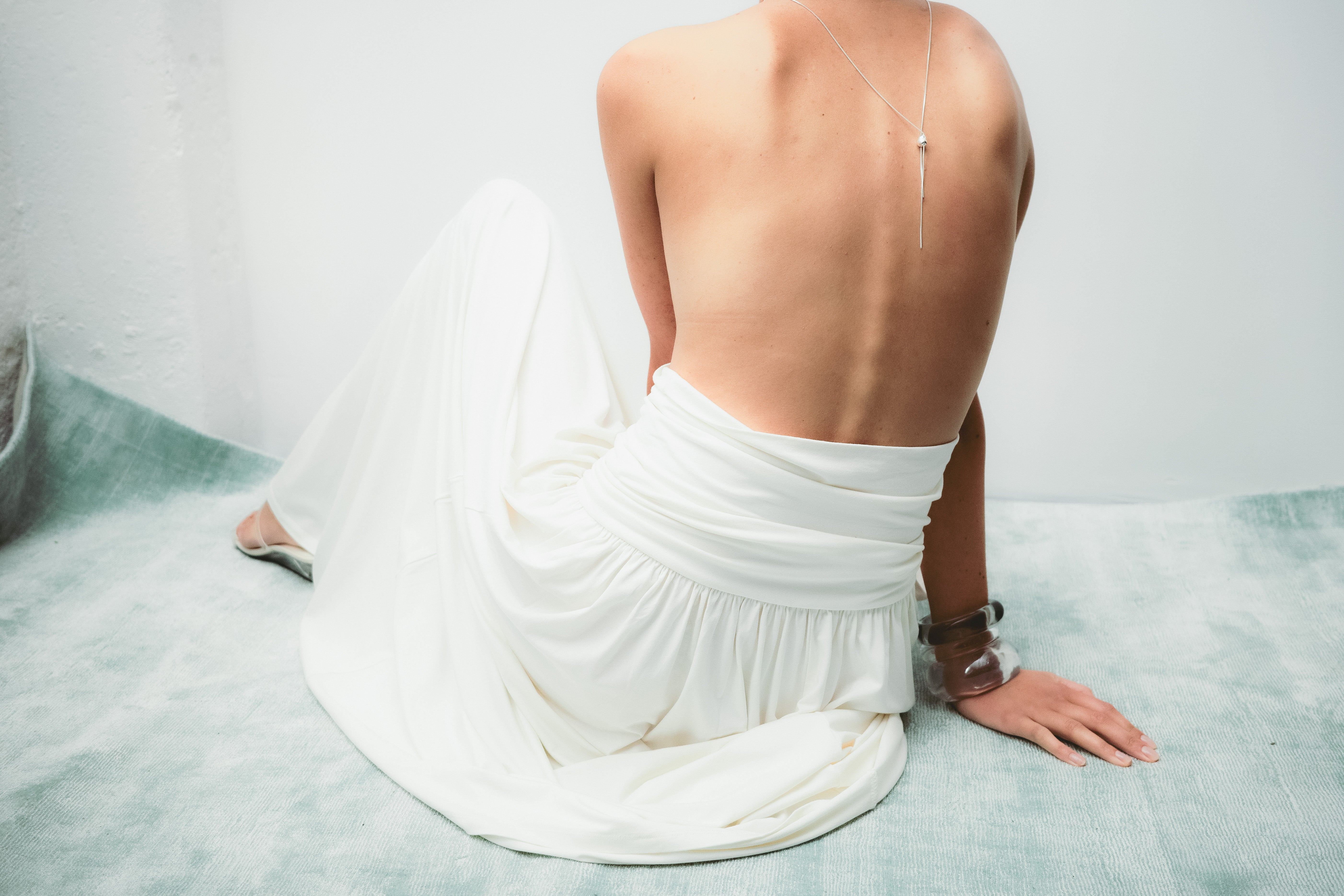 Person sitting on a bed wearing a white dress with a plain background